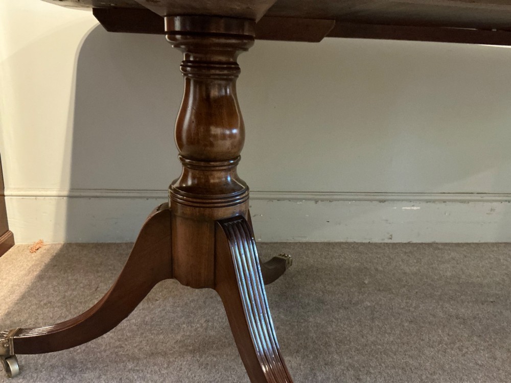 An antique mahogany twin pedestal dining table with rounded corners, extending leaves, turned supports, and splayed legs with brass castors. View XIV
