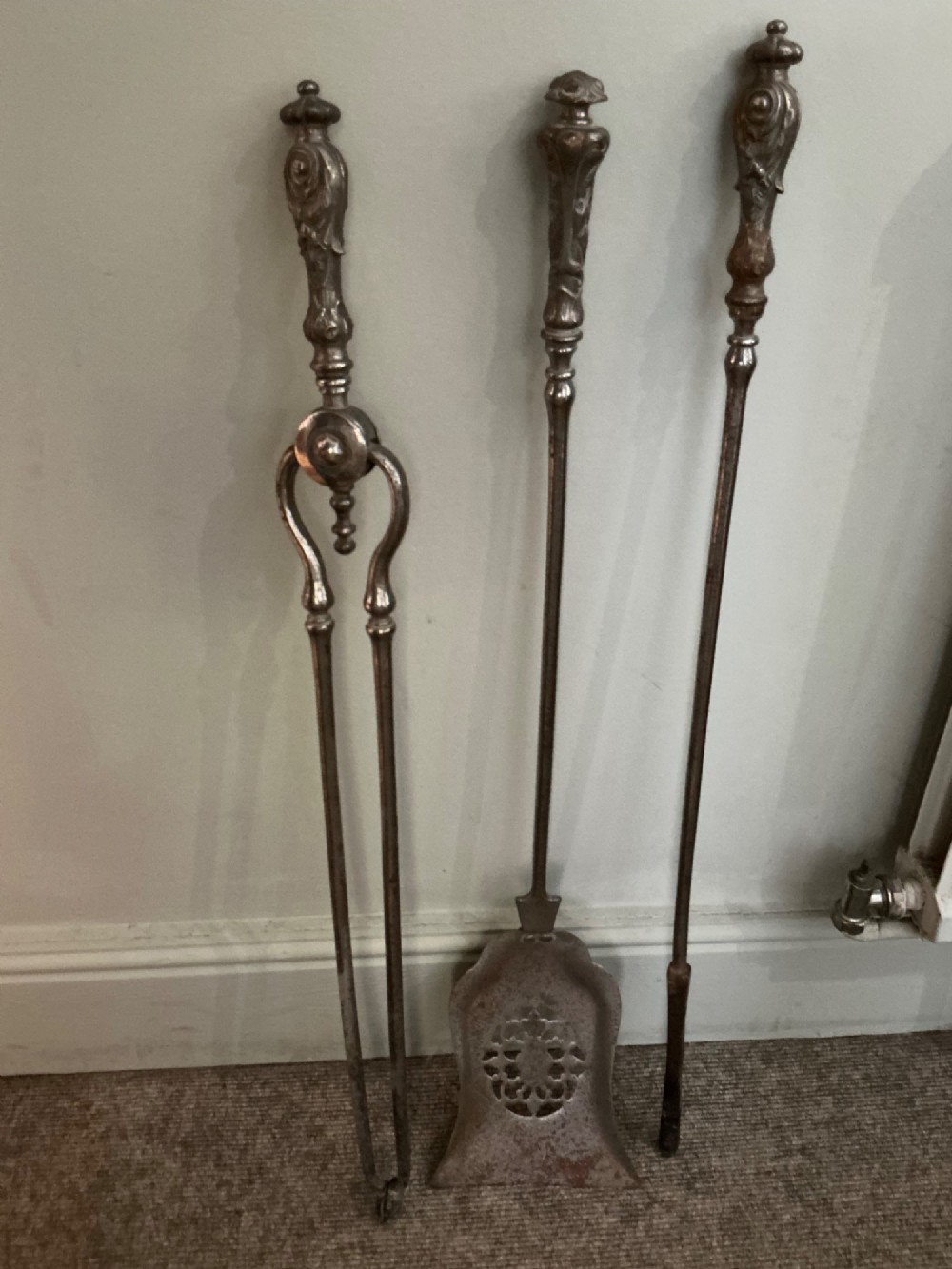 A three-piece set of polished steel fire tools including tongs, a poker, and a shovel with a pierced decorative blade.