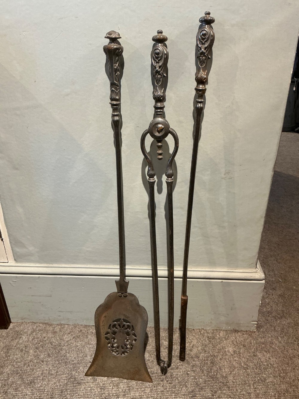 A three-piece set of polished steel fire tools including tongs, a poker, and a shovel with a pierced decorative blade. View II