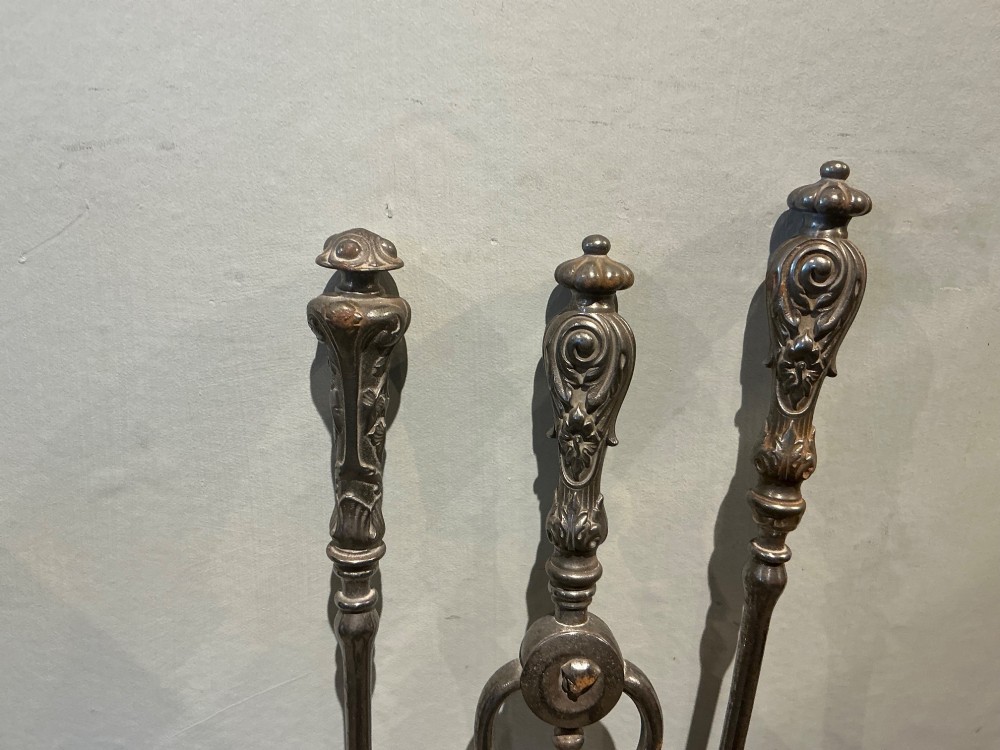 A three-piece set of polished steel fire tools including tongs, a poker, and a shovel with a pierced decorative blade. View III