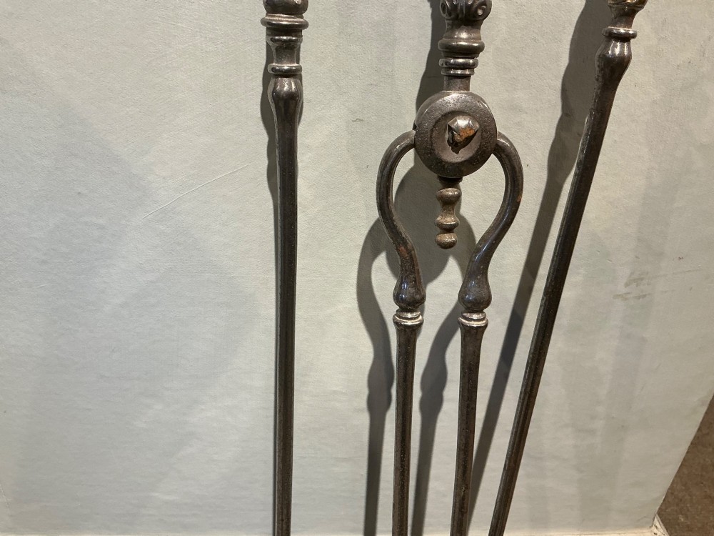 A three-piece set of polished steel fire tools including tongs, a poker, and a shovel with a pierced decorative blade. View IV