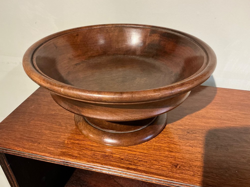 A turned wooden antique treen pedestal bowl with a polished finish and stepped circular base.