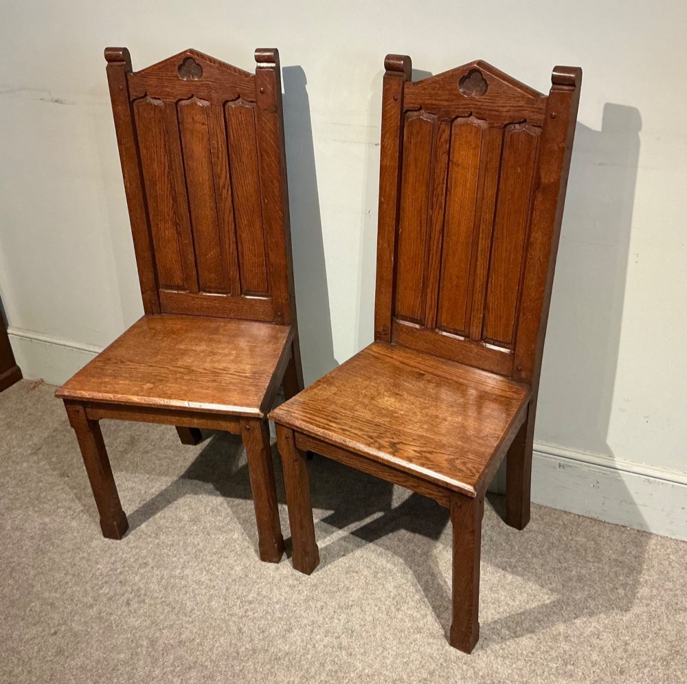 A pair of solid oak hall chairs featuring carved Gothic arches, trefoil back detailing, and flat wood seats. View II