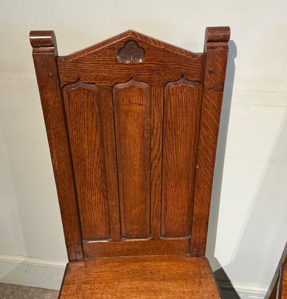 A pair of solid oak hall chairs featuring carved Gothic arches, trefoil back detailing, and flat wood seats. View III