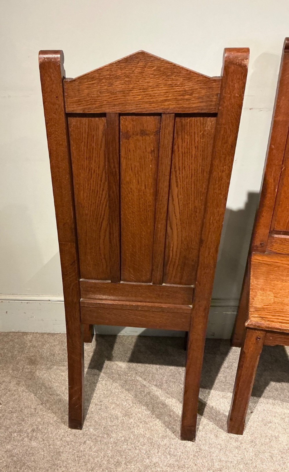 A pair of solid oak hall chairs featuring carved Gothic arches, trefoil back detailing, and flat wood seats. View VI