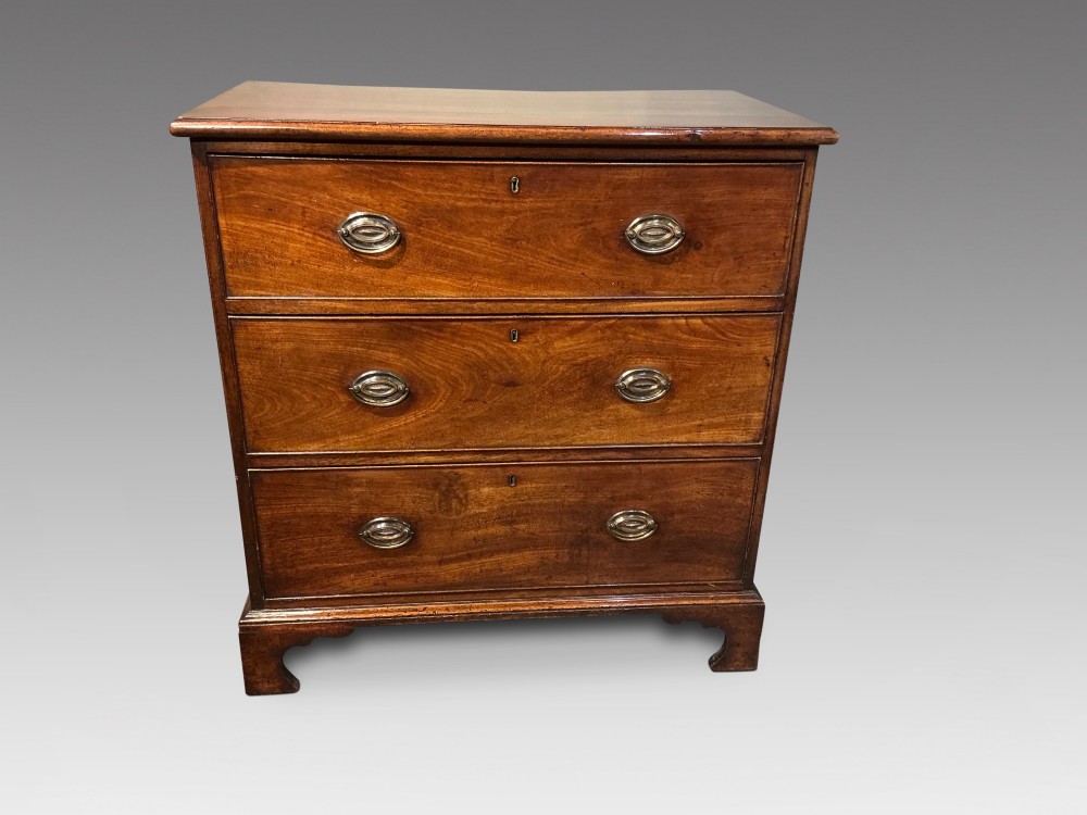 A Georgian mahogany chest of drawers with three graduated drawers, oval brass drop handles, and bracket feet.