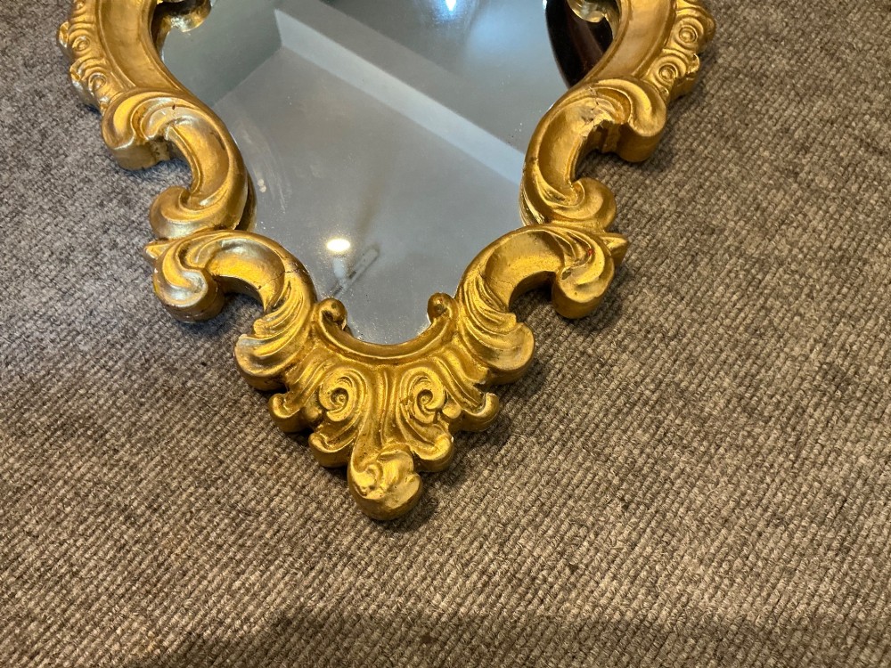 A cartouche-shaped wall mirror featuring a carved gold gilt frame with ornate C-scrolls and decorative flourishes. View III