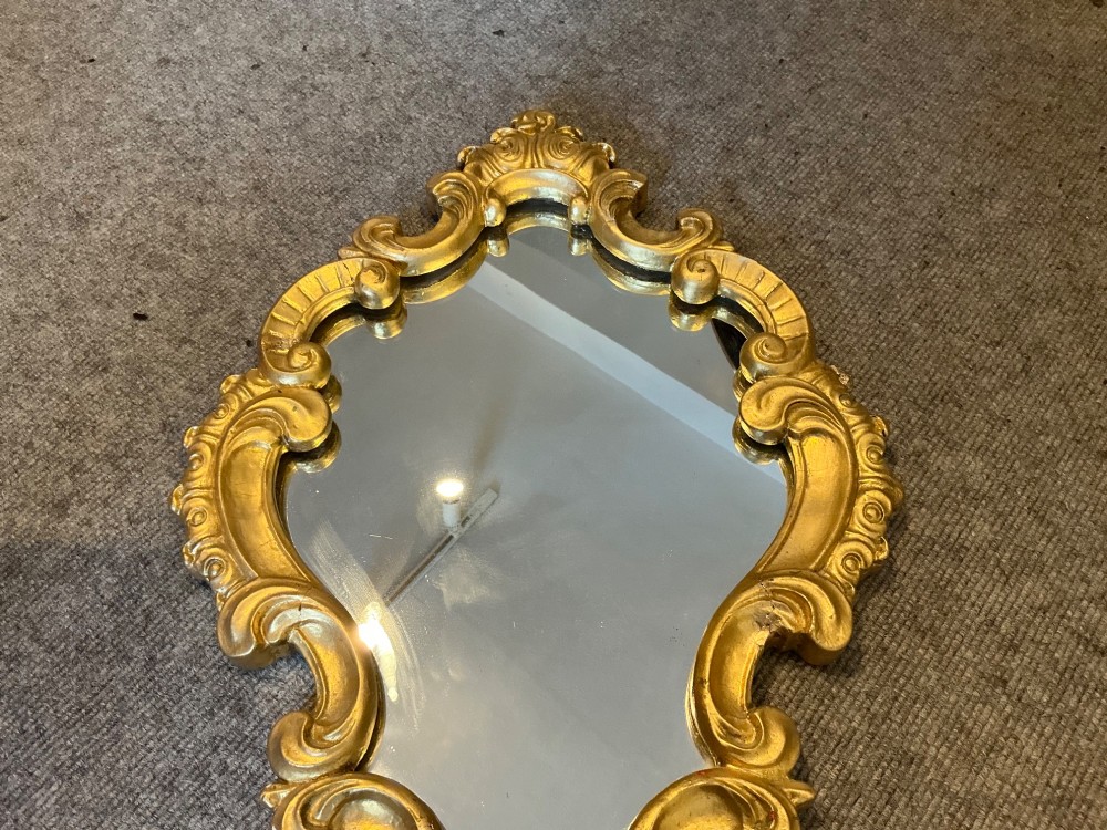 A cartouche-shaped wall mirror featuring a carved gold gilt frame with ornate C-scrolls and decorative flourishes. View IV