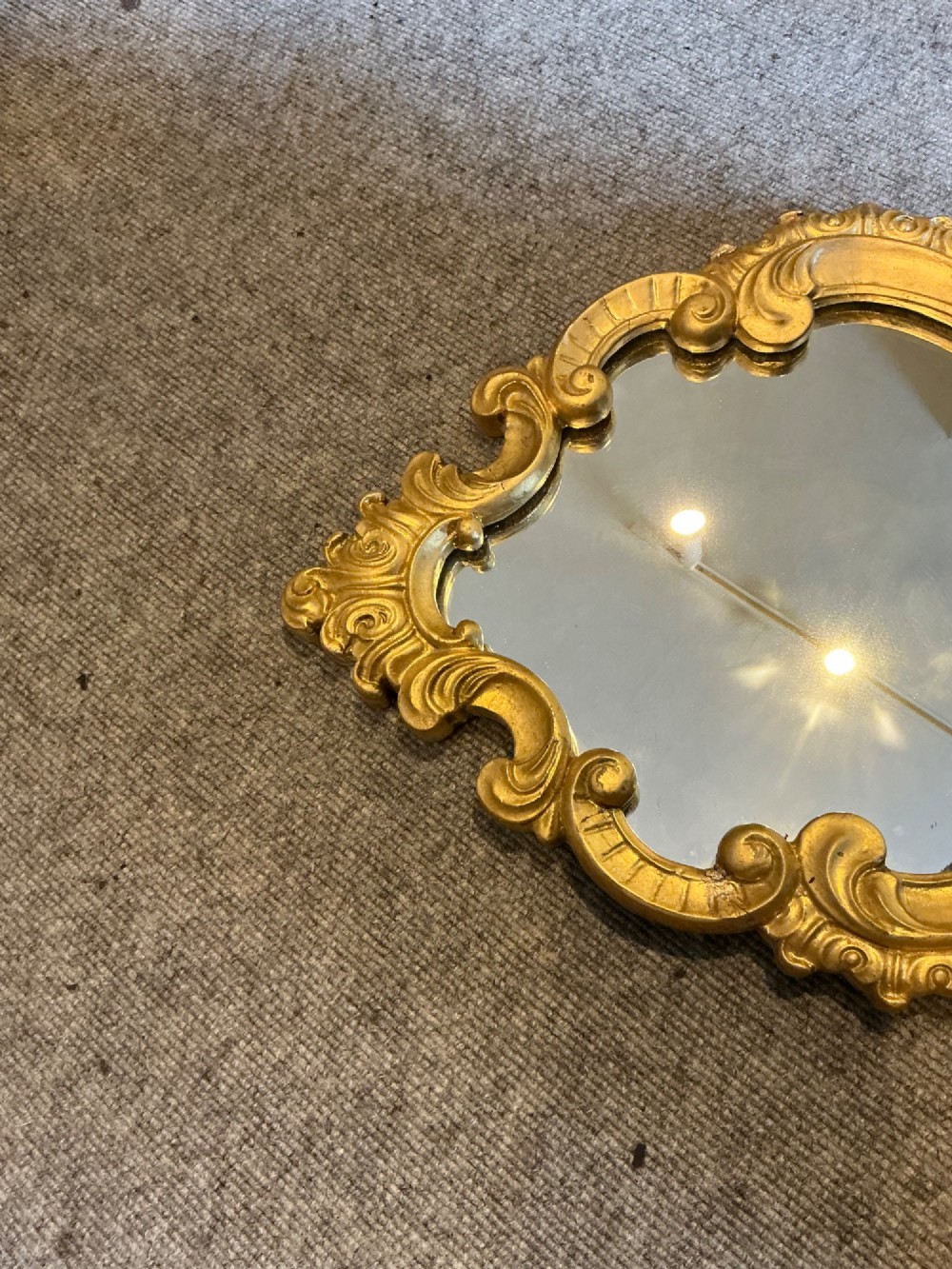 A cartouche-shaped wall mirror featuring a carved gold gilt frame with ornate C-scrolls and decorative flourishes. View V