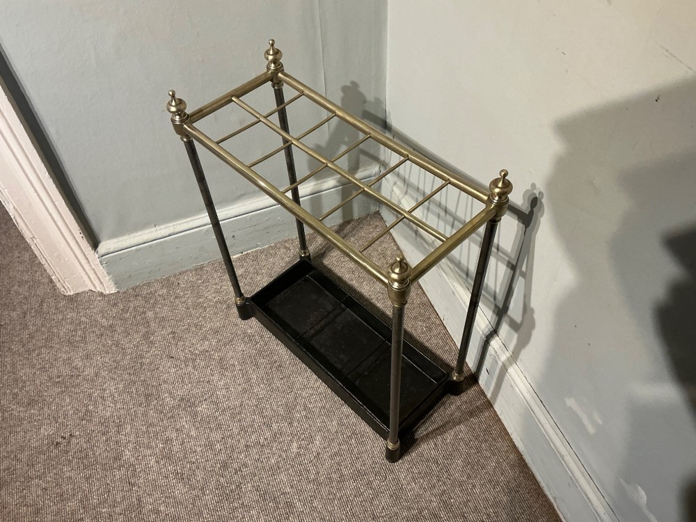 An antique brass and steel stick stand featuring a six-section top grid, urn finials, tubular uprights, and a black cast iron drip tray base. View II