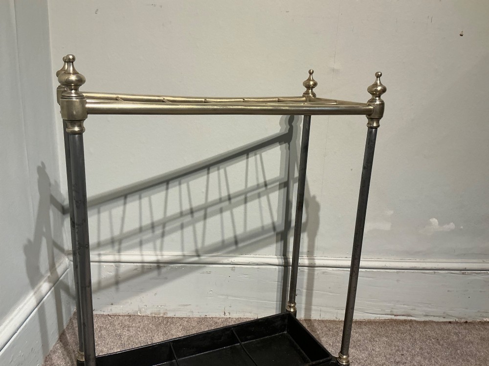 An antique brass and steel stick stand featuring a six-section top grid, urn finials, tubular uprights, and a black cast iron drip tray base. View IV