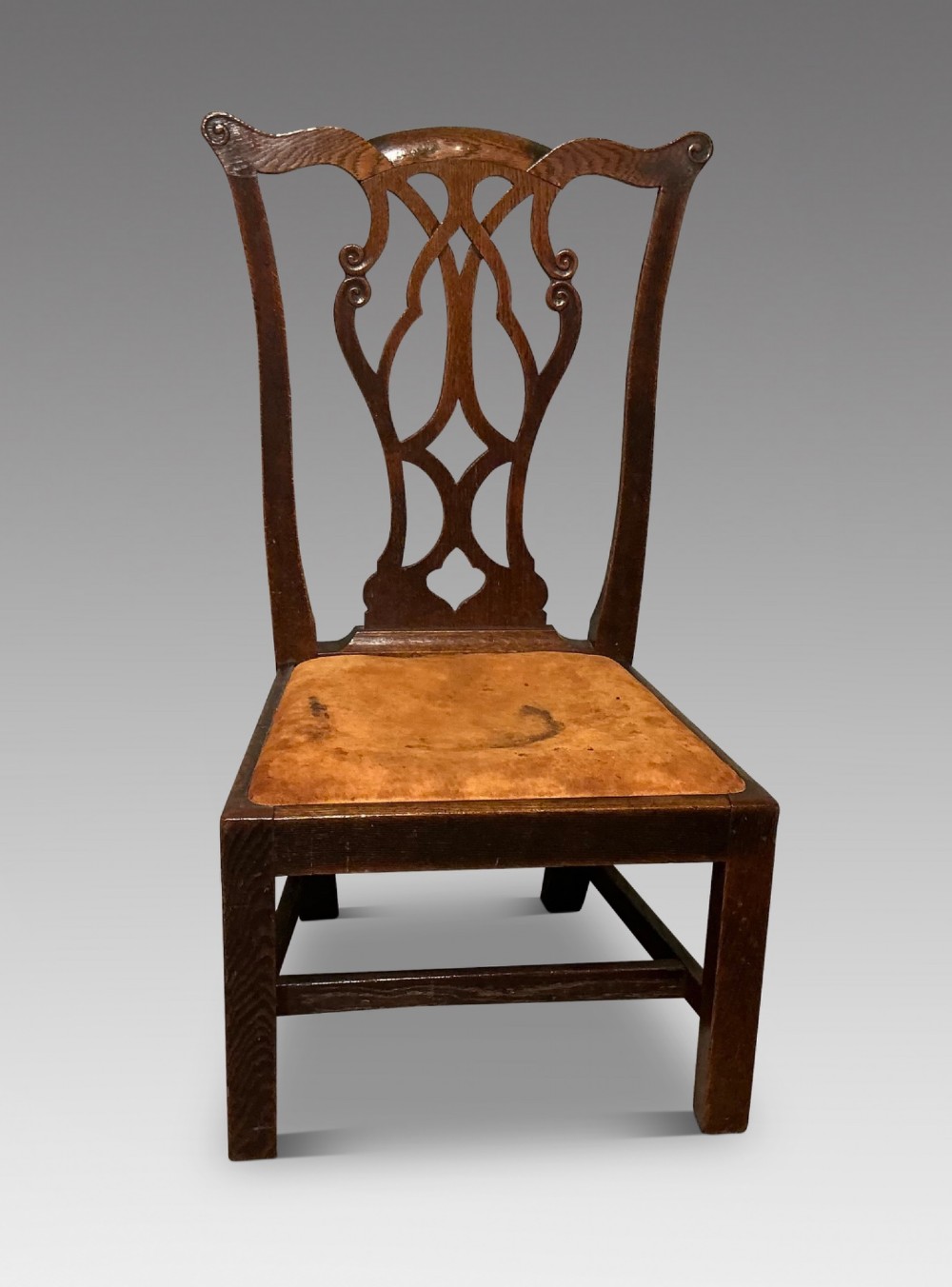 An antique dark oak side chair with an intricate pierced scroll splat back and a light brown upholstered drop-in seat.