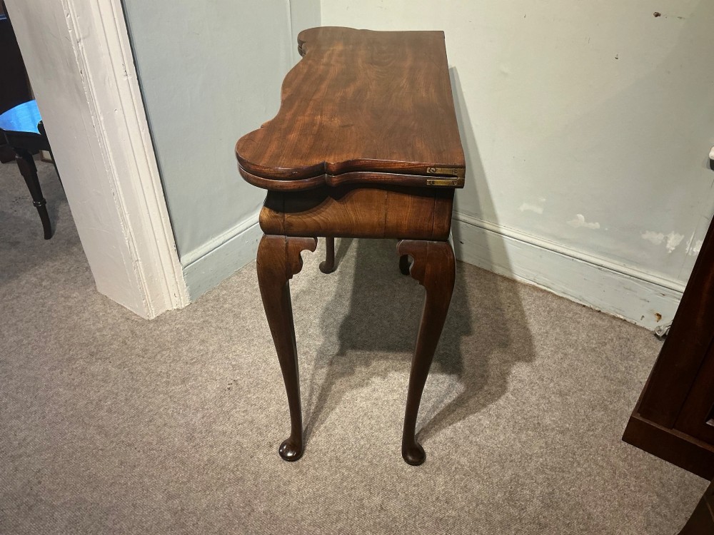 A Georgian walnut folding card table featuring a serpentine front, cabriole legs with pad feet, and brass handles. View VI