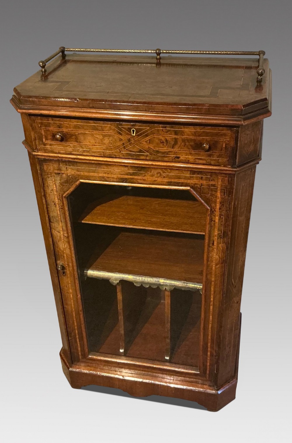 A Victorian burr walnut music cabinet featuring inlaid boxwood stringing, a top drawer, a glazed door revealing internal shelves and vertical dividers, and a brass gallery rail.