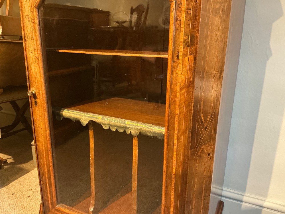 A Victorian burr walnut music cabinet featuring inlaid boxwood stringing, a top drawer, a glazed door revealing internal shelves and vertical dividers, and a brass gallery rail. View IV