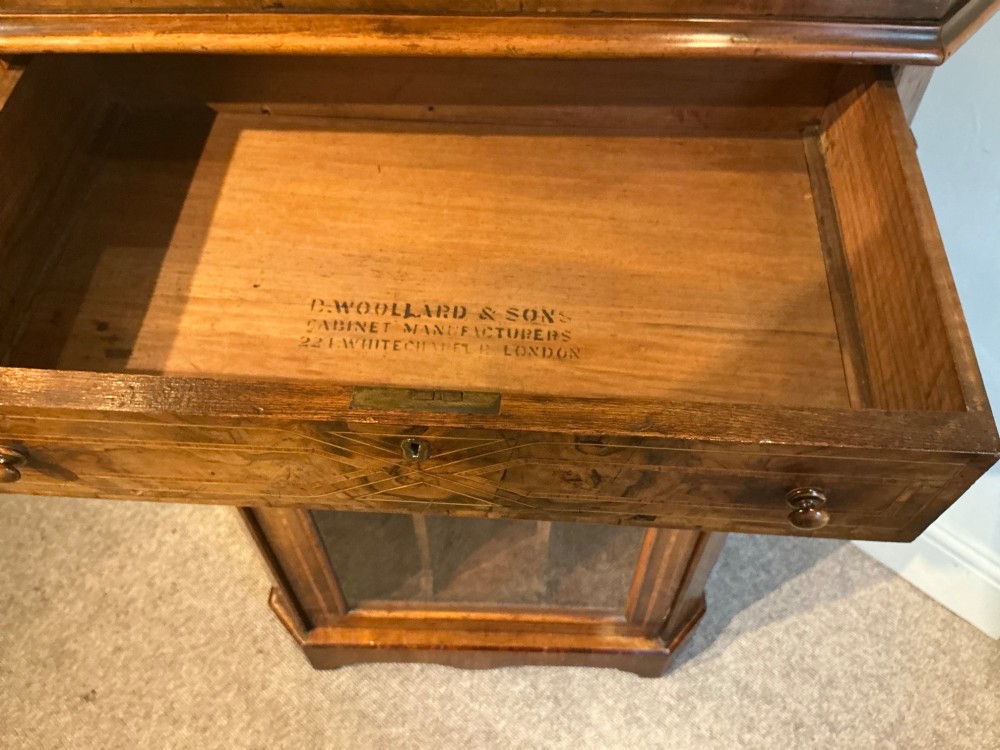 A Victorian burr walnut music cabinet featuring inlaid boxwood stringing, a top drawer, a glazed door revealing internal shelves and vertical dividers, and a brass gallery rail. View VII