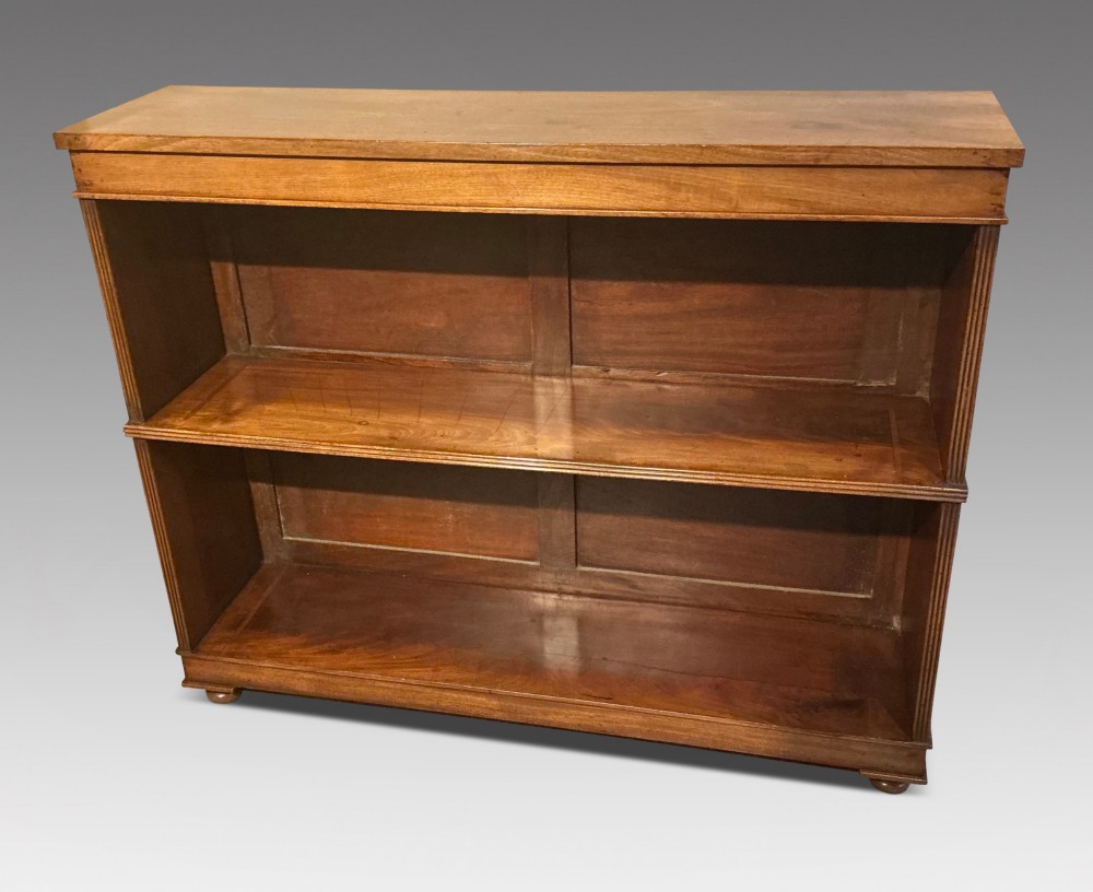 A low open mahogany bookcase featuring two wide shelves, reeded side pilasters, a panelled back, and low turned feet.
