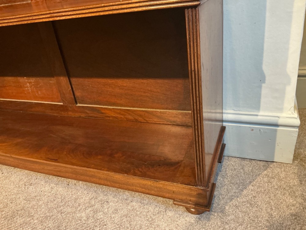 A low open mahogany bookcase featuring two wide shelves, reeded side pilasters, a panelled back, and low turned feet. View VI