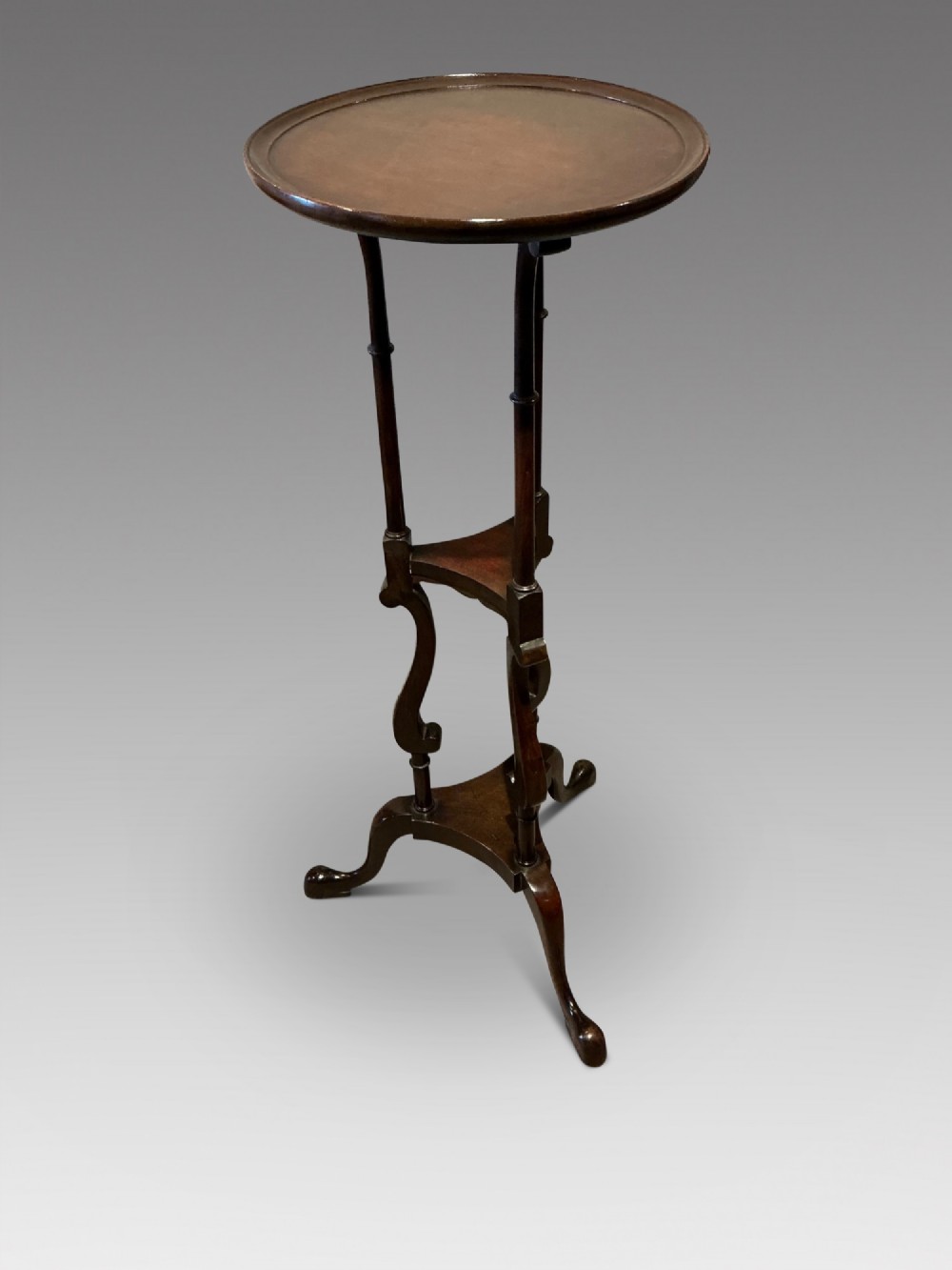 A dark mahogany torchere featuring a circular dished top supported by slender uprights, scroll details, and a tripod base with pad feet.