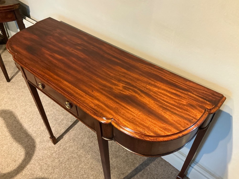 An antique mahogany hall table featuring a serpentine front, a single central drawer with brass ring handles, and four tapered square legs ending in spade feet. View III