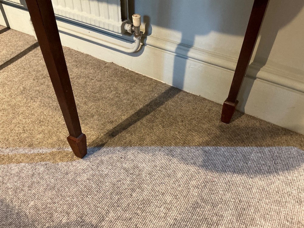 An antique mahogany hall table featuring a serpentine front, a single central drawer with brass ring handles, and four tapered square legs ending in spade feet. View V