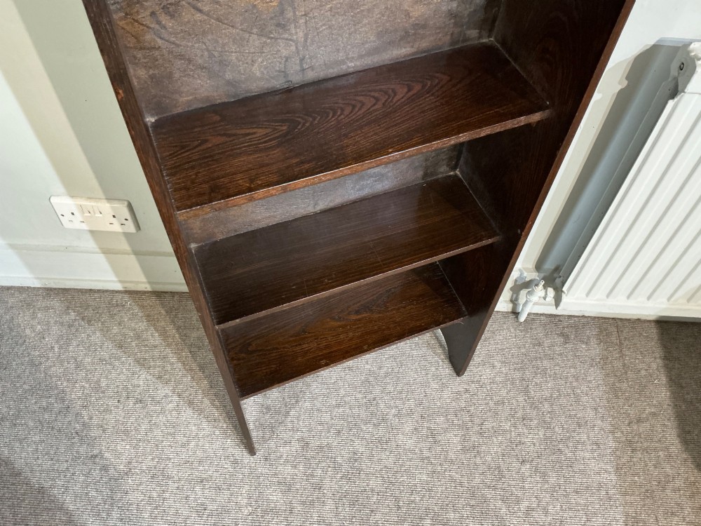 An antique dark oak open bookcase featuring four fixed shelves, cutout side panels forming feet, and a curved top cresting rail. View III