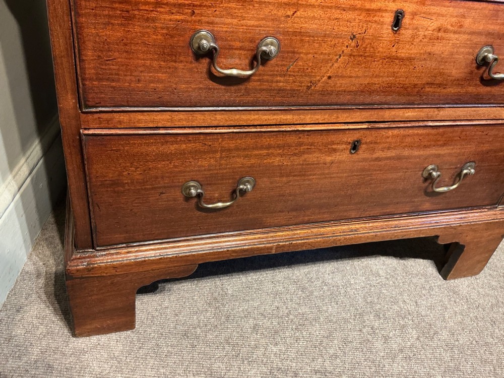 A Georgian mahogany chest of drawers featuring four graduated drawers with brass swan-neck handles and bracket feet. View V