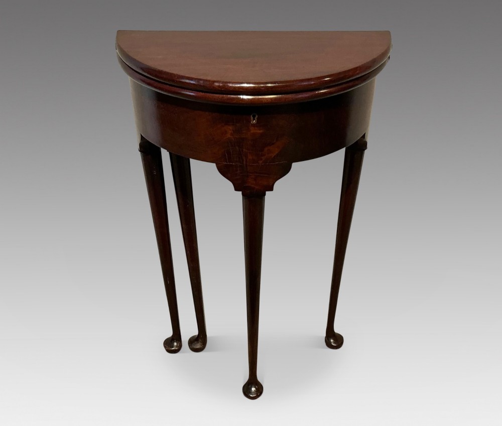 A dark mahogany demi-lune fold-over tea table with slender tapered legs, pad feet, and a brass keyhole escutcheon on the apron.