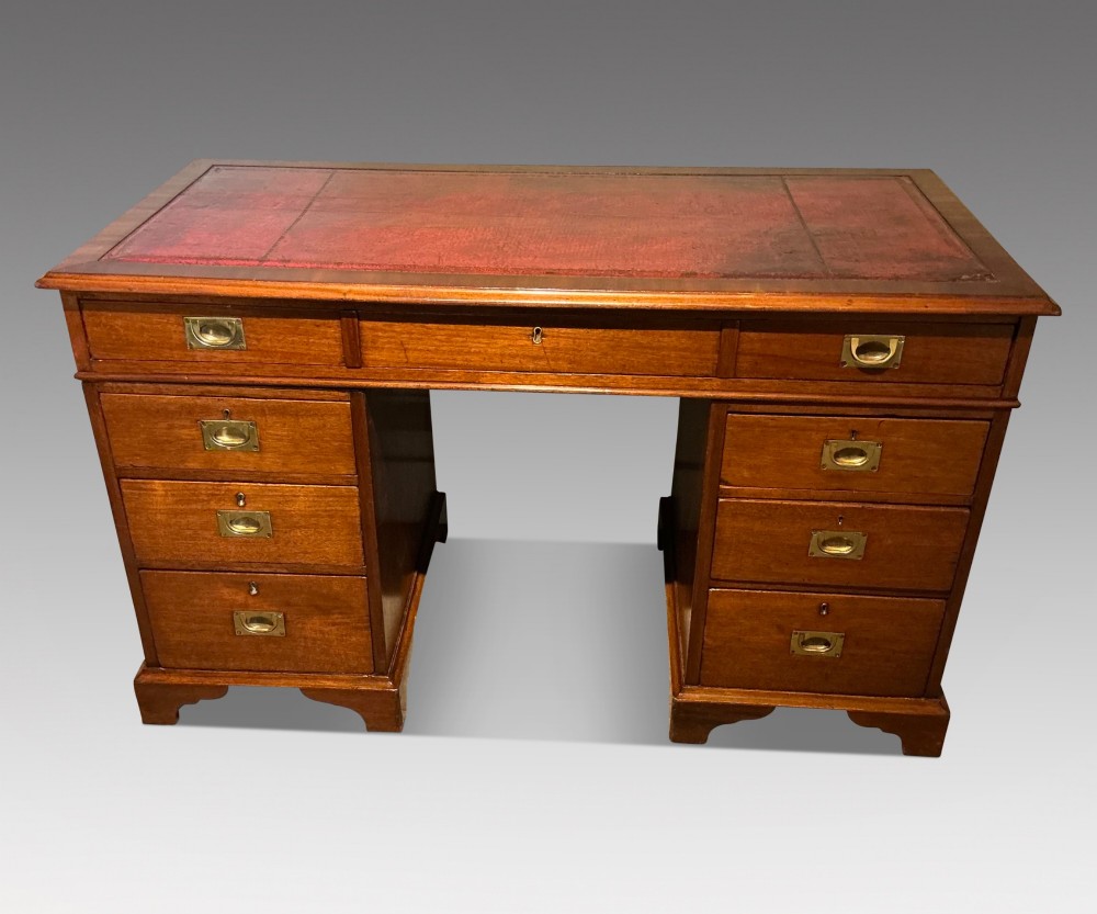 An antique mahogany pedestal desk featuring a red leather inset top, brass campaign drawer handles, and three drawers on each pedestal.