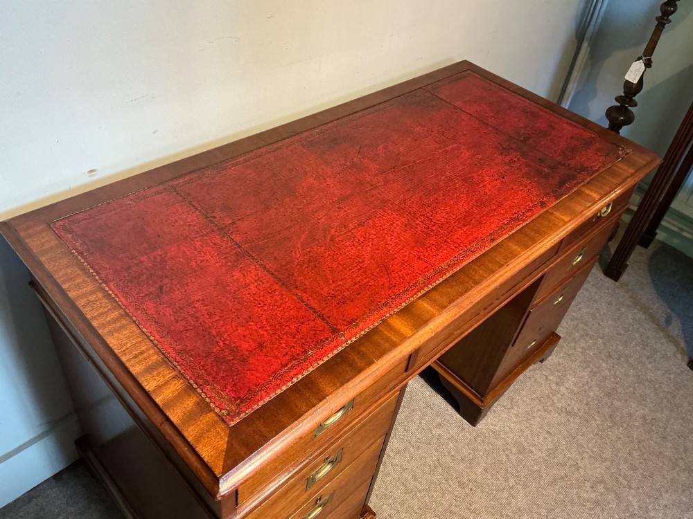 An antique mahogany pedestal desk featuring a red leather inset top, brass campaign drawer handles, and three drawers on each pedestal. View III