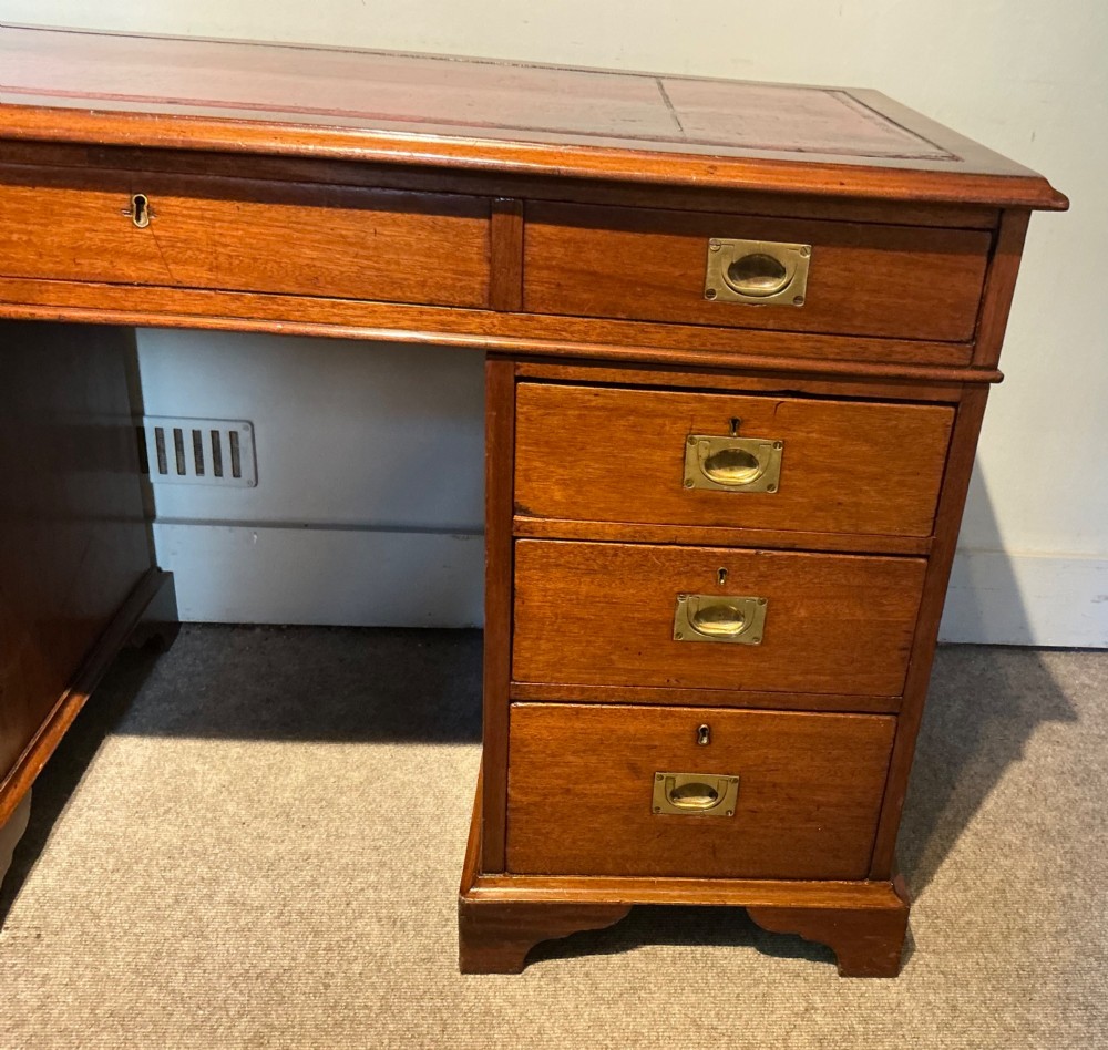 An antique mahogany pedestal desk featuring a red leather inset top, brass campaign drawer handles, and three drawers on each pedestal. View IV