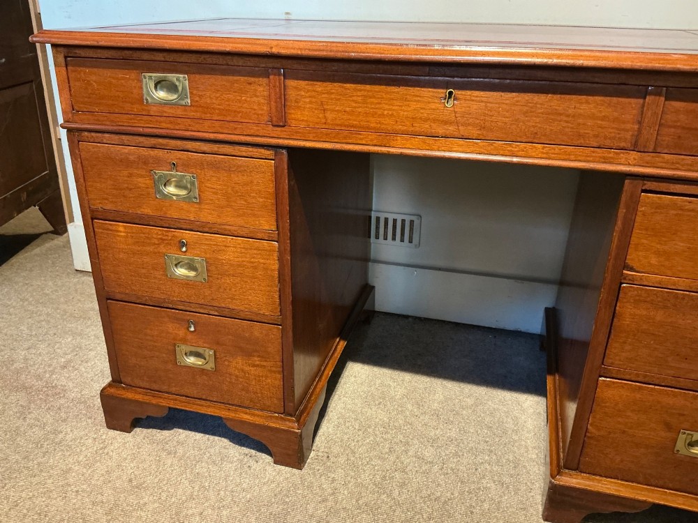 An antique mahogany pedestal desk featuring a red leather inset top, brass campaign drawer handles, and three drawers on each pedestal. View V