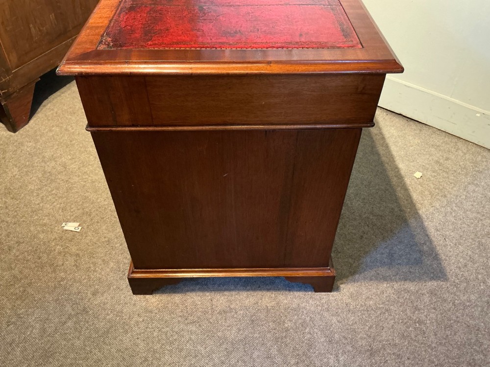 An antique mahogany pedestal desk featuring a red leather inset top, brass campaign drawer handles, and three drawers on each pedestal. View VI