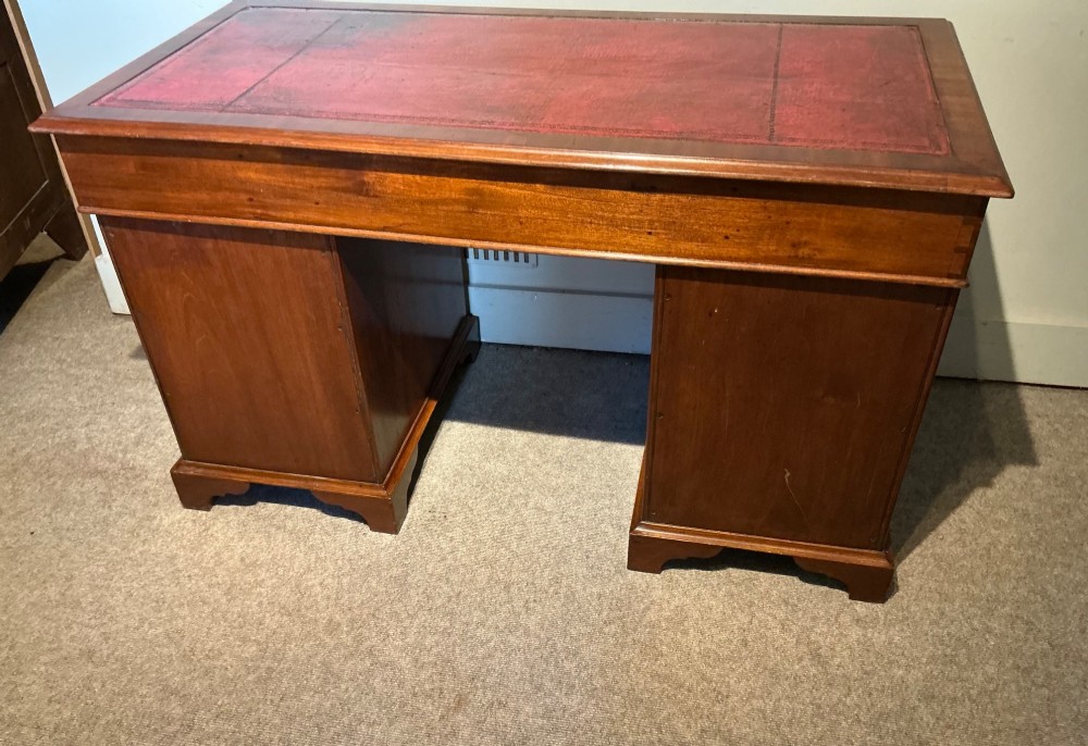 An antique mahogany pedestal desk featuring a red leather inset top, brass campaign drawer handles, and three drawers on each pedestal. View VII