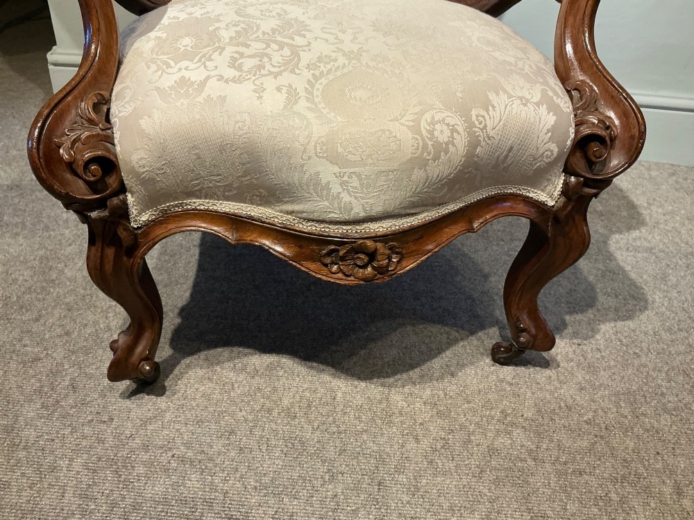 A Victorian high-back armchair featuring a carved dark wood frame, deep button-tufted cream damask upholstery, and cabriole legs on brass castors. View III