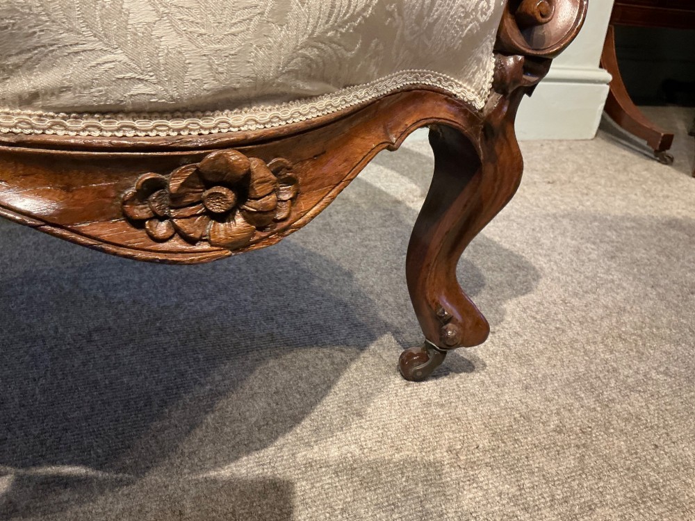 A Victorian high-back armchair featuring a carved dark wood frame, deep button-tufted cream damask upholstery, and cabriole legs on brass castors. View VII