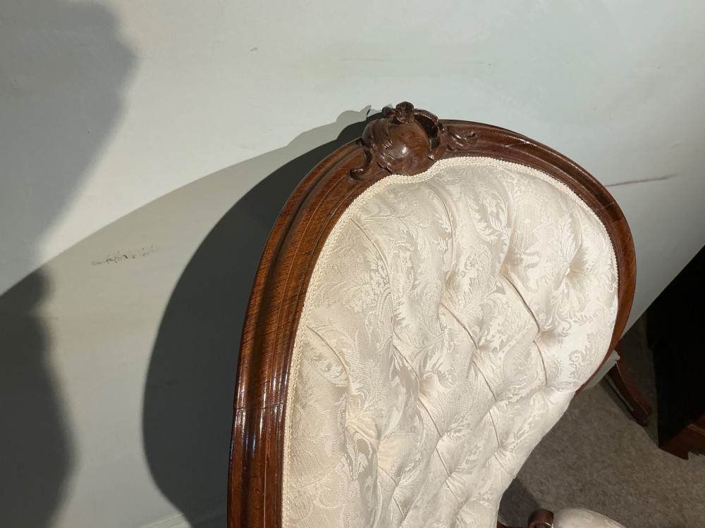 A Victorian high-back armchair featuring a carved dark wood frame, deep button-tufted cream damask upholstery, and cabriole legs on brass castors. View VIII