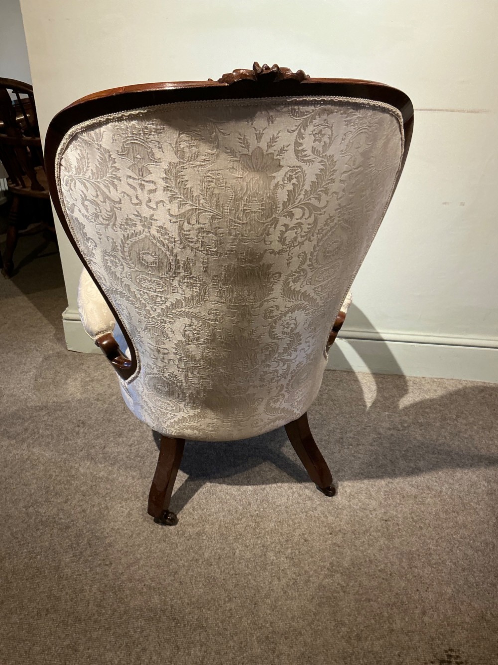 A Victorian high-back armchair featuring a carved dark wood frame, deep button-tufted cream damask upholstery, and cabriole legs on brass castors. View X