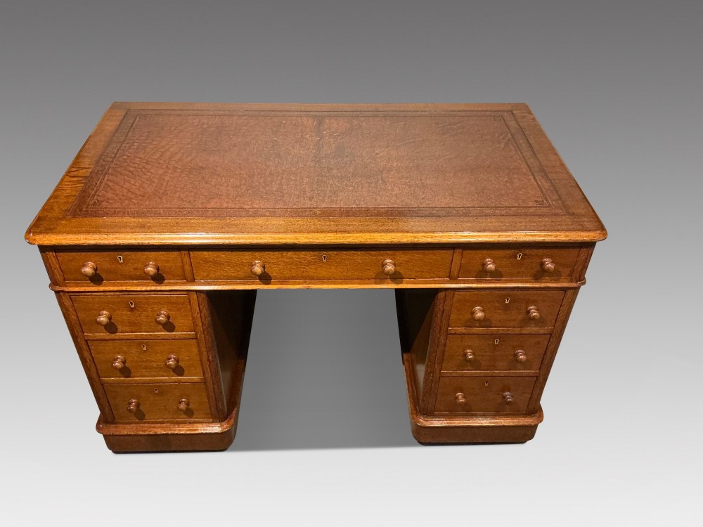 An antique oak pedestal desk featuring a rectangular leather inset top, nine drawers with turned wooden knobs, and twin plinth bases. View II