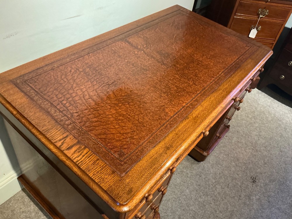 An antique oak pedestal desk featuring a rectangular leather inset top, nine drawers with turned wooden knobs, and twin plinth bases. View III
