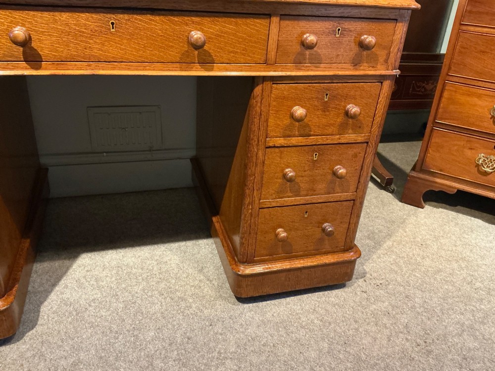 An antique oak pedestal desk featuring a rectangular leather inset top, nine drawers with turned wooden knobs, and twin plinth bases. View VI