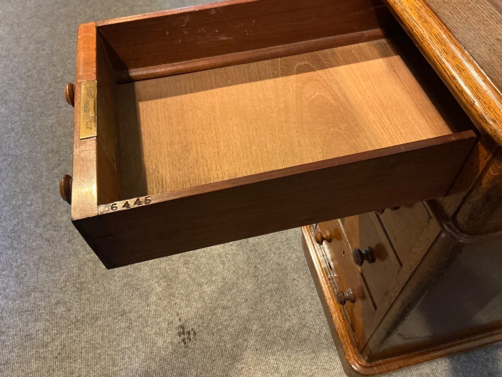 An antique oak pedestal desk featuring a rectangular leather inset top, nine drawers with turned wooden knobs, and twin plinth bases. View VII