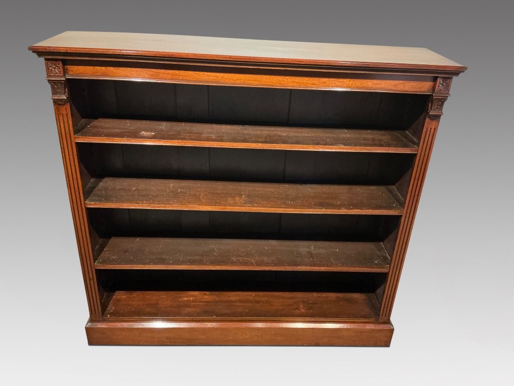 An antique mahogany open bookcase featuring four fixed shelves, fluted side pilasters with carved rosette capitals, and a solid plinth base.