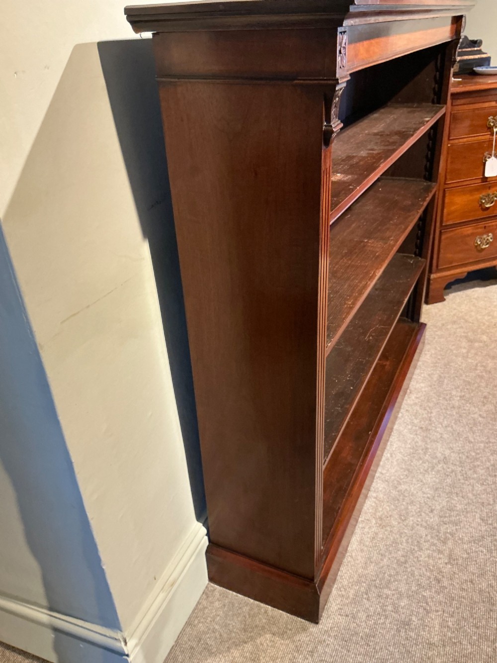 An antique mahogany open bookcase featuring four fixed shelves, fluted side pilasters with carved rosette capitals, and a solid plinth base. View V