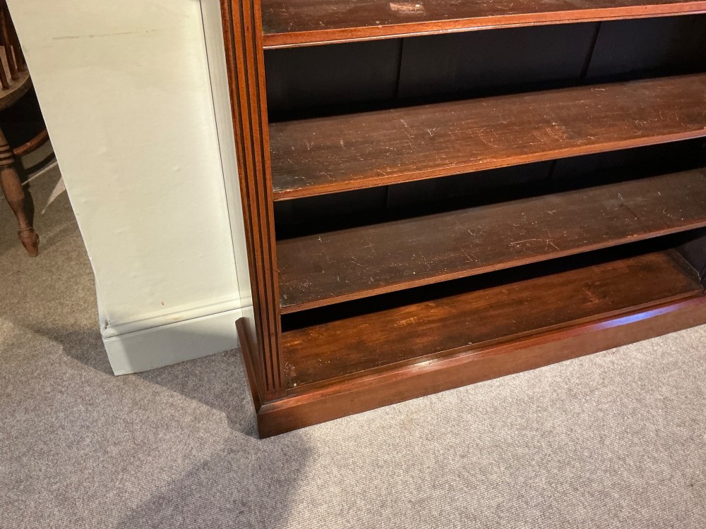 An antique mahogany open bookcase featuring four fixed shelves, fluted side pilasters with carved rosette capitals, and a solid plinth base. View VI