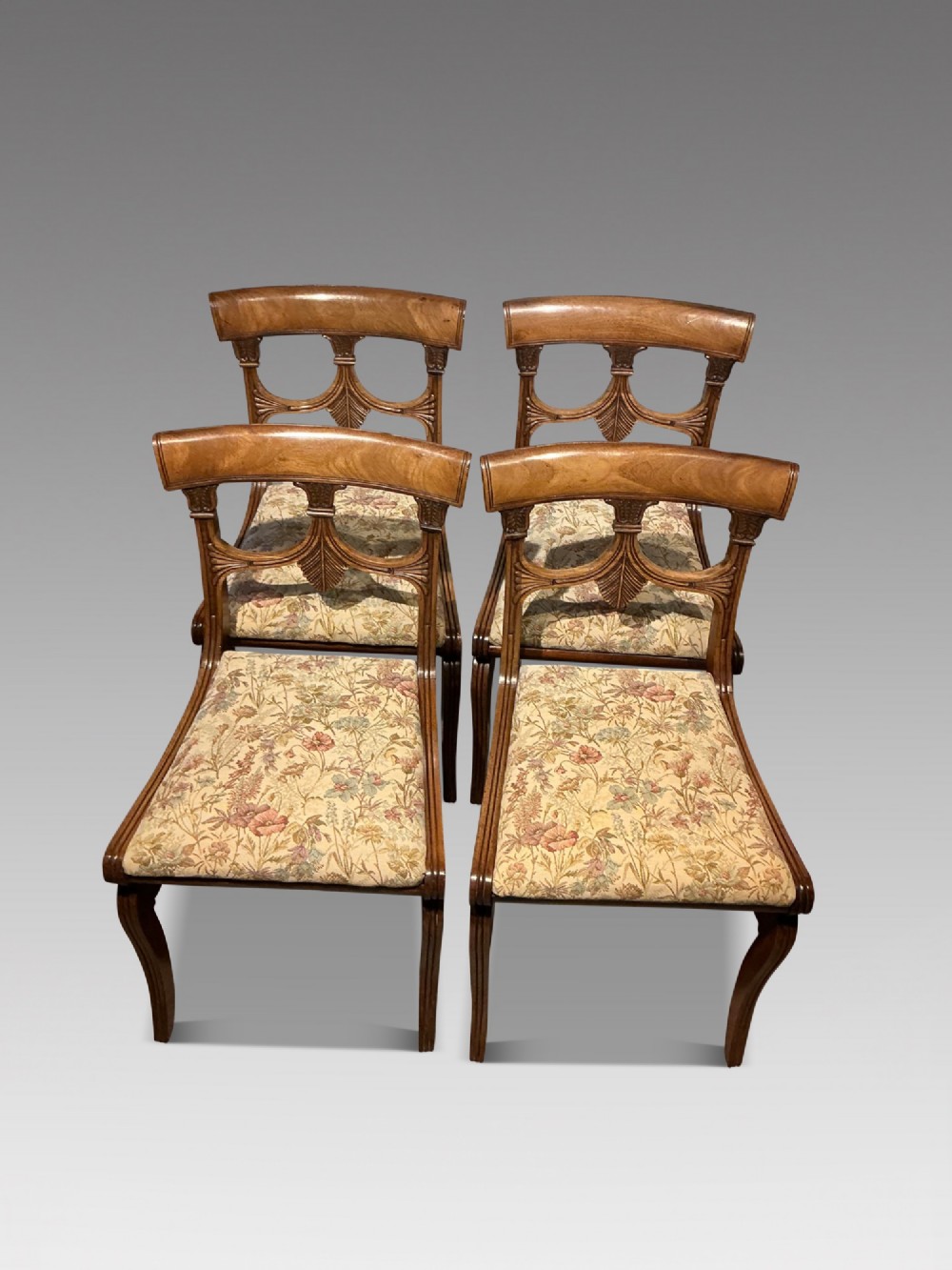 A set of four antique mahogany dining chairs with carved palmette back splats, curved crest rails, sabre legs, and floral tapestry upholstered drop-in seats. View II