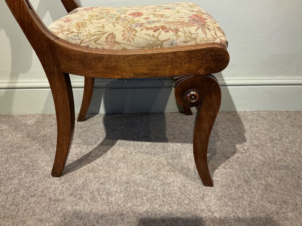A set of four antique mahogany dining chairs with carved palmette back splats, curved crest rails, sabre legs, and floral tapestry upholstered drop-in seats. View V