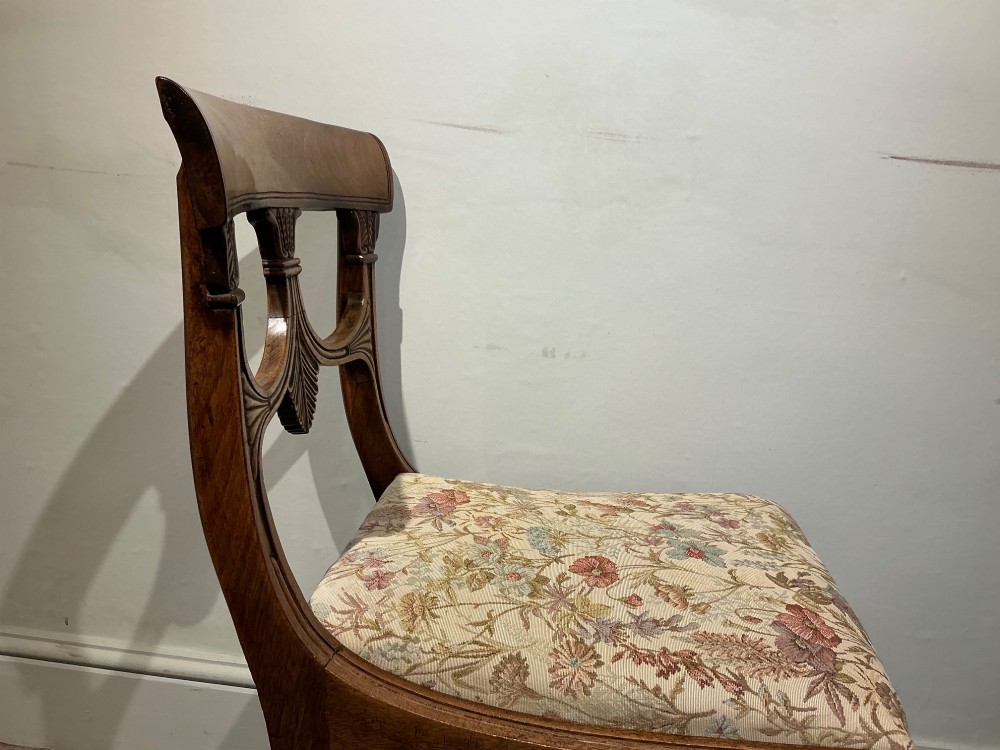 A set of four antique mahogany dining chairs with carved palmette back splats, curved crest rails, sabre legs, and floral tapestry upholstered drop-in seats. View VI