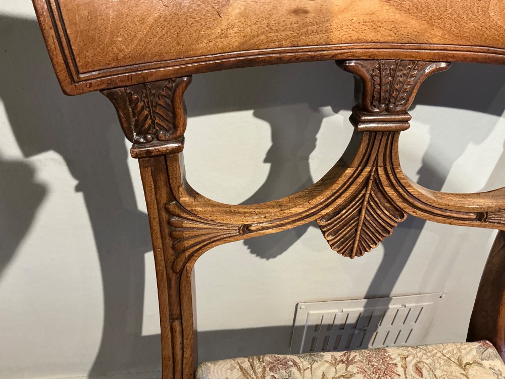 A set of four antique mahogany dining chairs with carved palmette back splats, curved crest rails, sabre legs, and floral tapestry upholstered drop-in seats. View IX