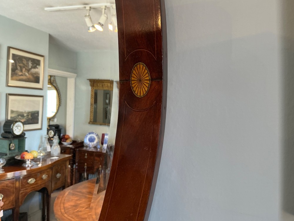 An antique oval mahogany wall mirror featuring a polished wooden frame accented with stringing inlay and four decorative marquetry medallions surrounding a bevelled mirror plate. View III